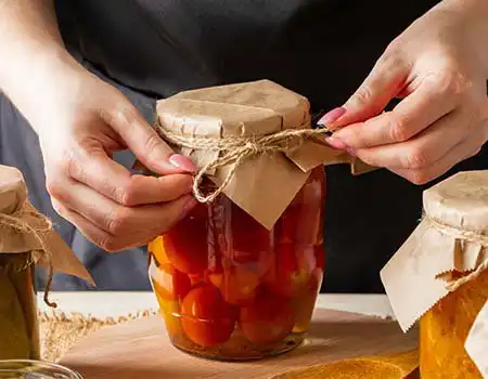 Mãos colocando vegetais cortados em pote com líquido de conserva
