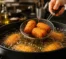 Chef realizando a técnica correta de fritura por imersão para obter alimentos dourados e crocantes.